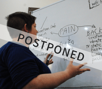 A picture of Jess Walton in front of a whiteboard with adjectives. Overlaid is the word "Postponed"