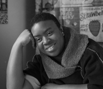 A black and white photo of Maxine Beneba Clarke. She is smiling contemplatively, her head resting on the back of one hand. 
