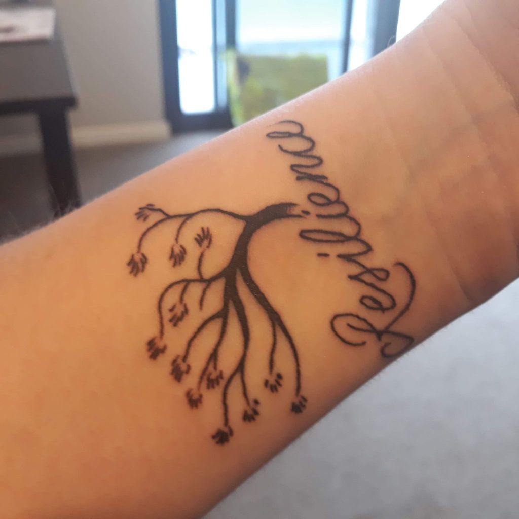 A photo of a person's tattooed forearm. The tattoo is of a skeleton-bare oak tree  with the word ‘Resilience’ inscribed in cursive underneath.