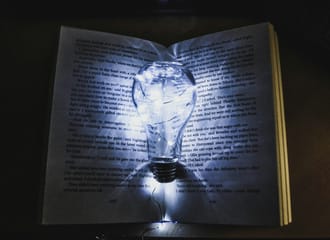 A photo of a book with a light globe between its pages lighting up the words.