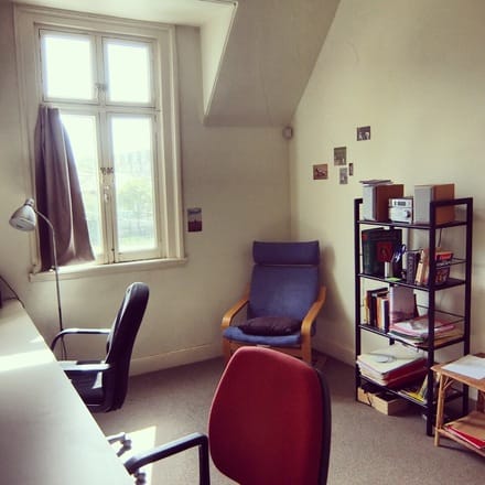 A photo of Studio 7 at Glenfern, with two chairs at a long desk, with an easy chair and bookshelf behind them