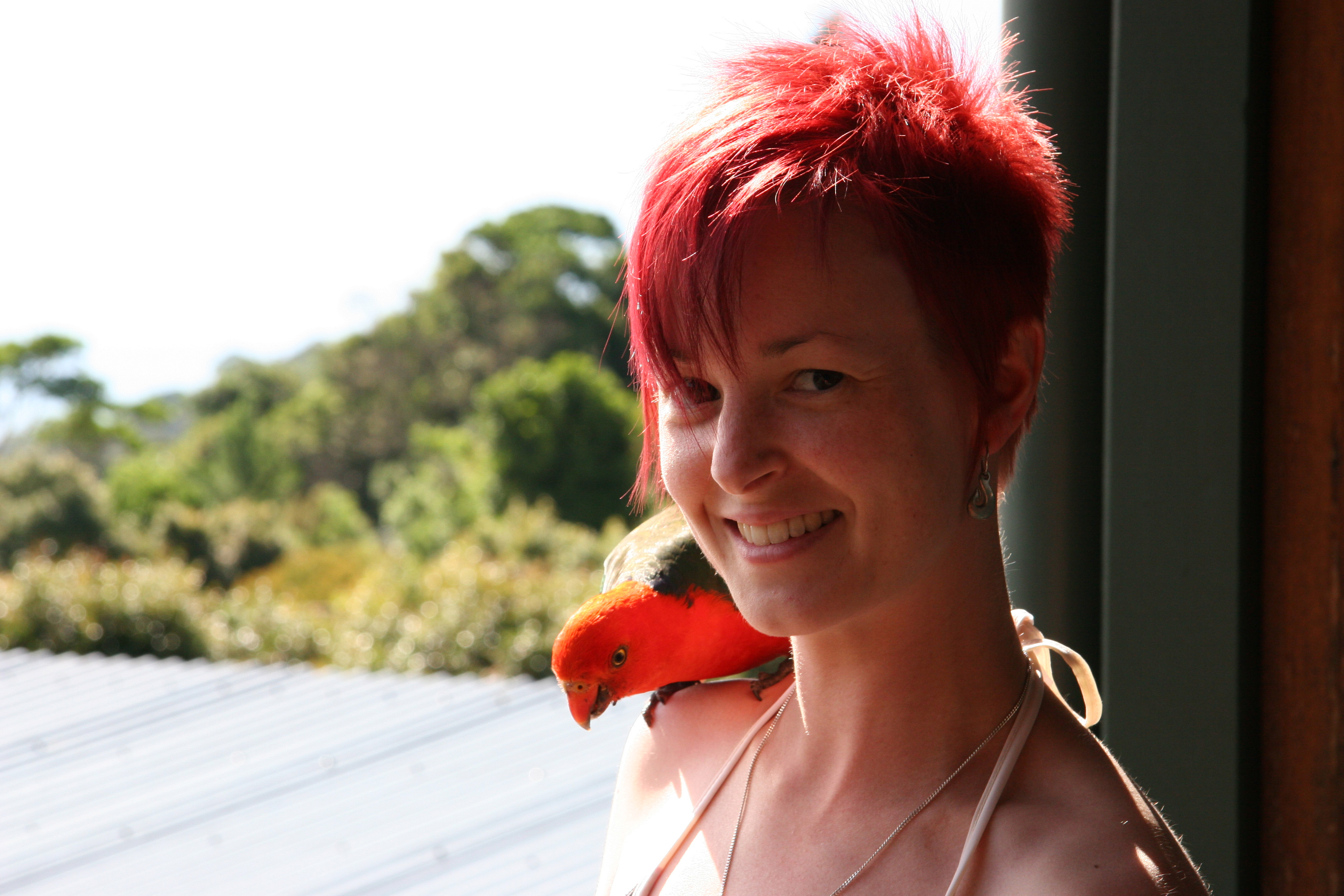 A portrait of Jessica Obersby, a woman with pale skin and bright red hair. She is smiling and has a little parrot on her shoulder
