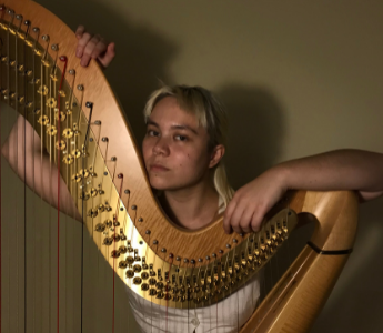 A portrait of Lou, a person with dark peach skin, blonde hair with a fringe and brown eyes. They are leaning on a harp