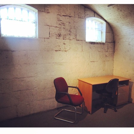 A photo of Studio 7 at Old Melbourne Gaol, featuring a curved, stone roof, a small empty desk and two chairs