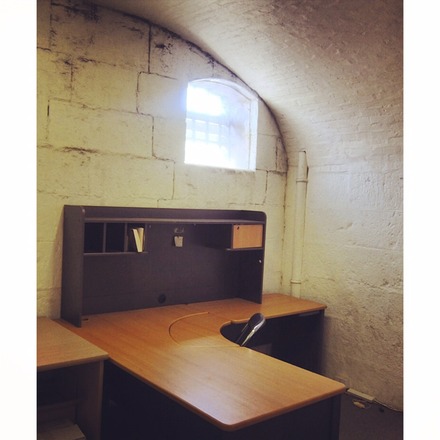 A photo of Studio 5 at Old Melbourne Gaol, featuring a single chair, a desk and one small, high window