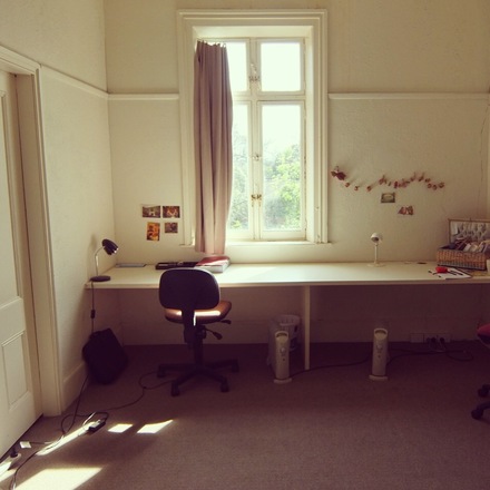 A photo of Studio 3 at Glenfern, with a long desk, lamp and single chair beneath a curtained window. 