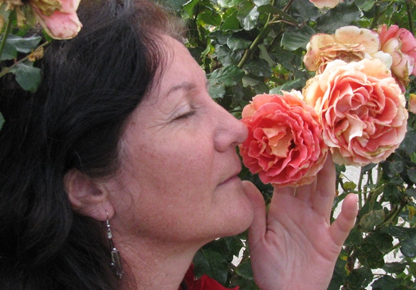 Side profile of Maribel, eyes closed smelling a tangerine coloured rose.