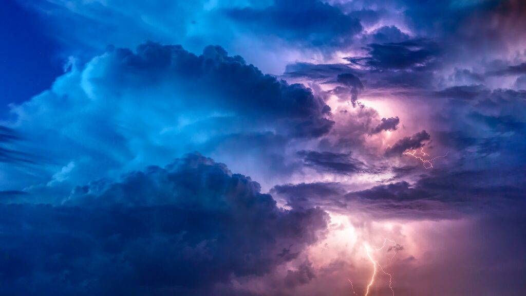 A photo of a cloudy sky with lightning strikes and streaks of light. The clouds and sky are moody and evocative, coloured in high-contrast blues and purples.
